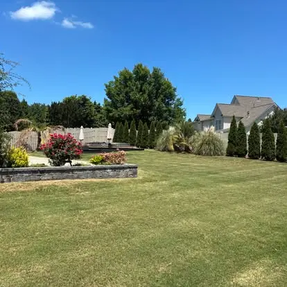 Landscaped backyard with a stone retaining wall, blooming shrubs, and a healthy green lawn in Greenville, SC