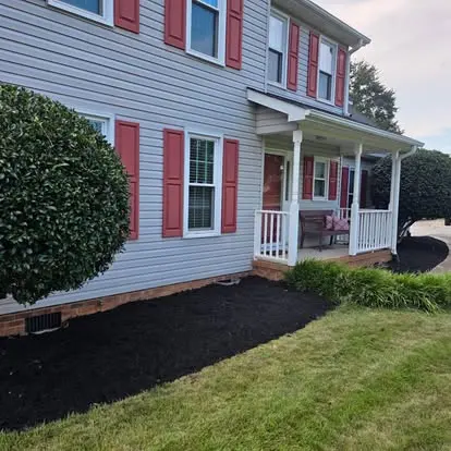 Fresh black mulch installed in a clean foundation bed at a gray home with red shutters in Greenville, SC